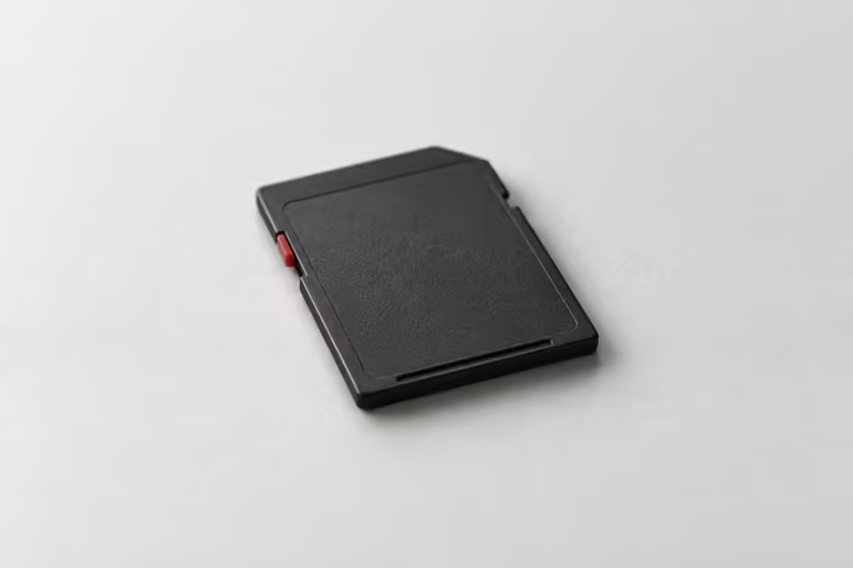 A single charcoal SD memory card lying on a grey surface, one small dark red tab on its side