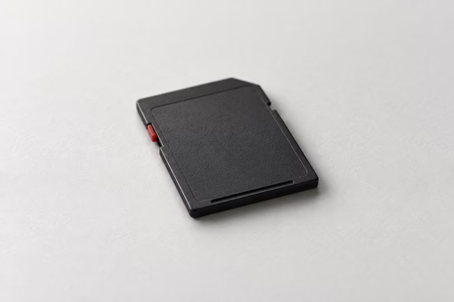 A single charcoal SD memory card lying on a grey surface, one small dark red tab on its side
