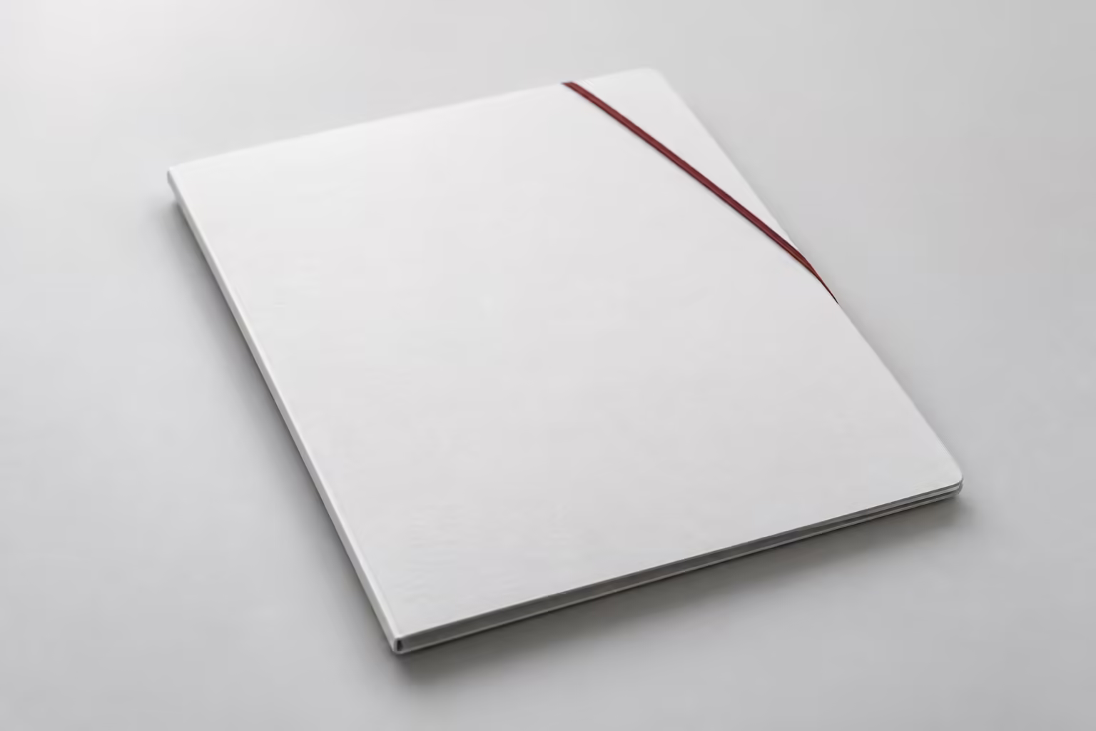 A closed white document folder lying flat on a grey surface, a thin dark red elastic band across one corner