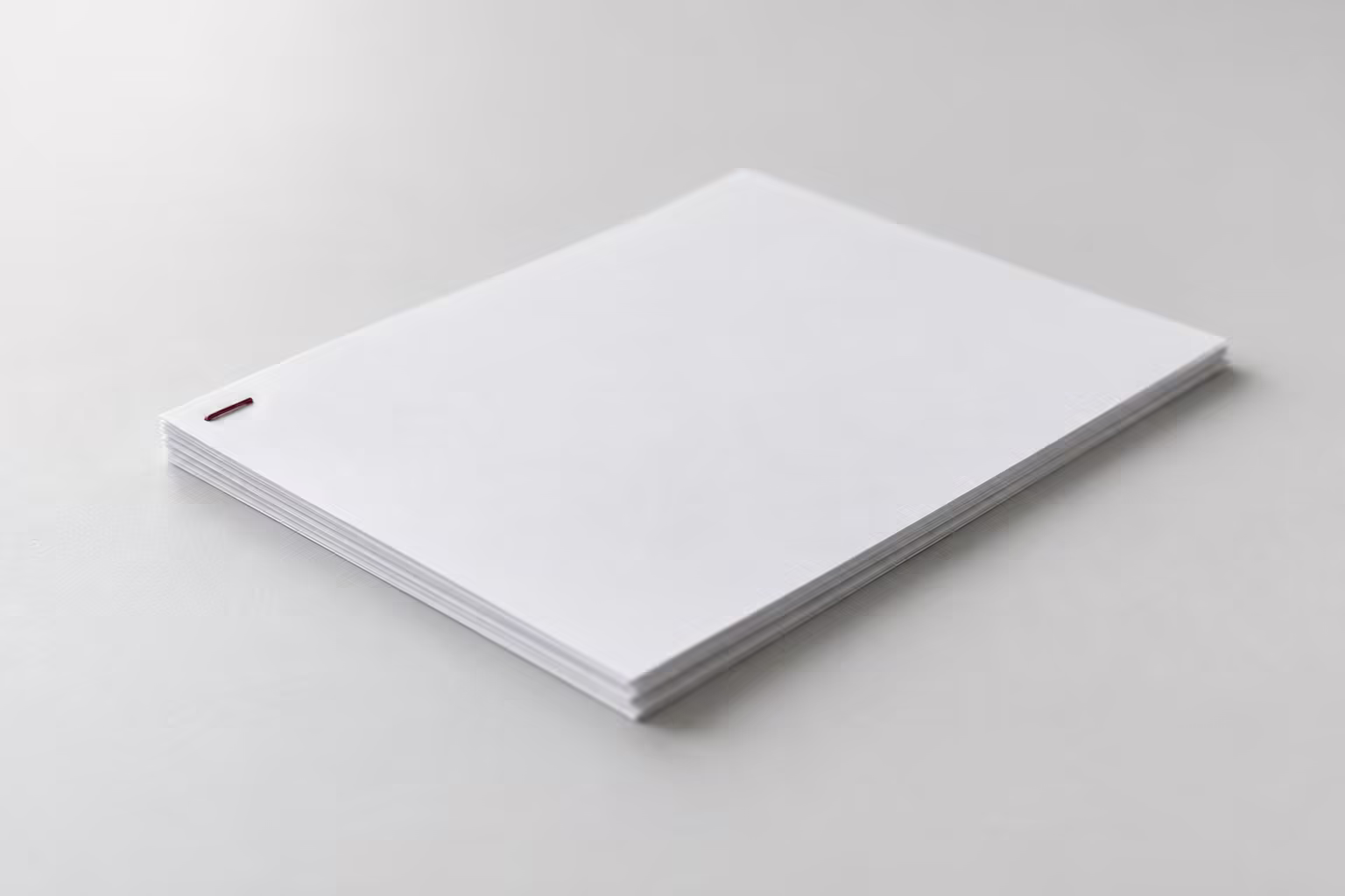A small sheaf of white paper stapled at one corner with a single dark red staple, on a grey surface