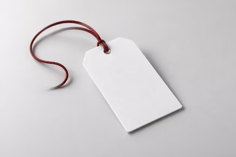 A blank white luggage tag on a grey surface with a thin dark red cord loop